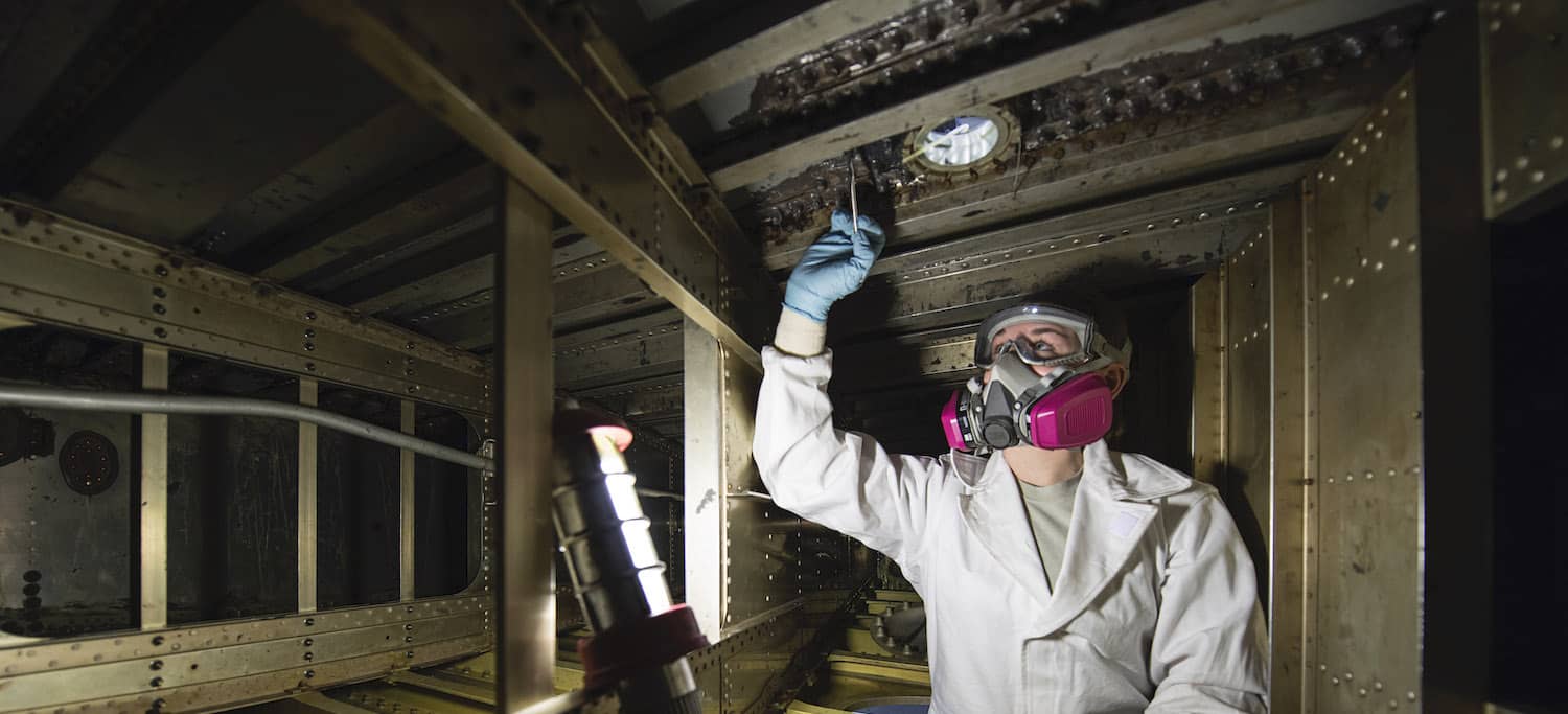 U.S. Department of Defense worker inspecting a fuel tank system for microbial corrosion.